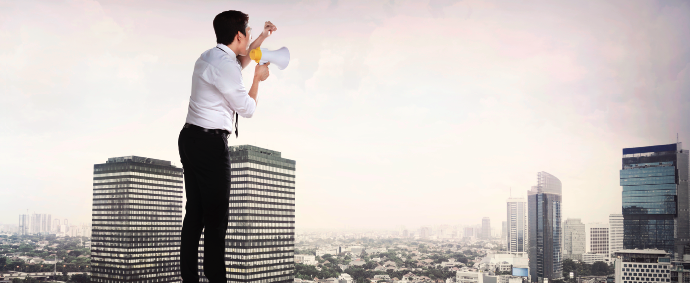 Businessman yelling through a bullhorn from the roof of a skyscraper